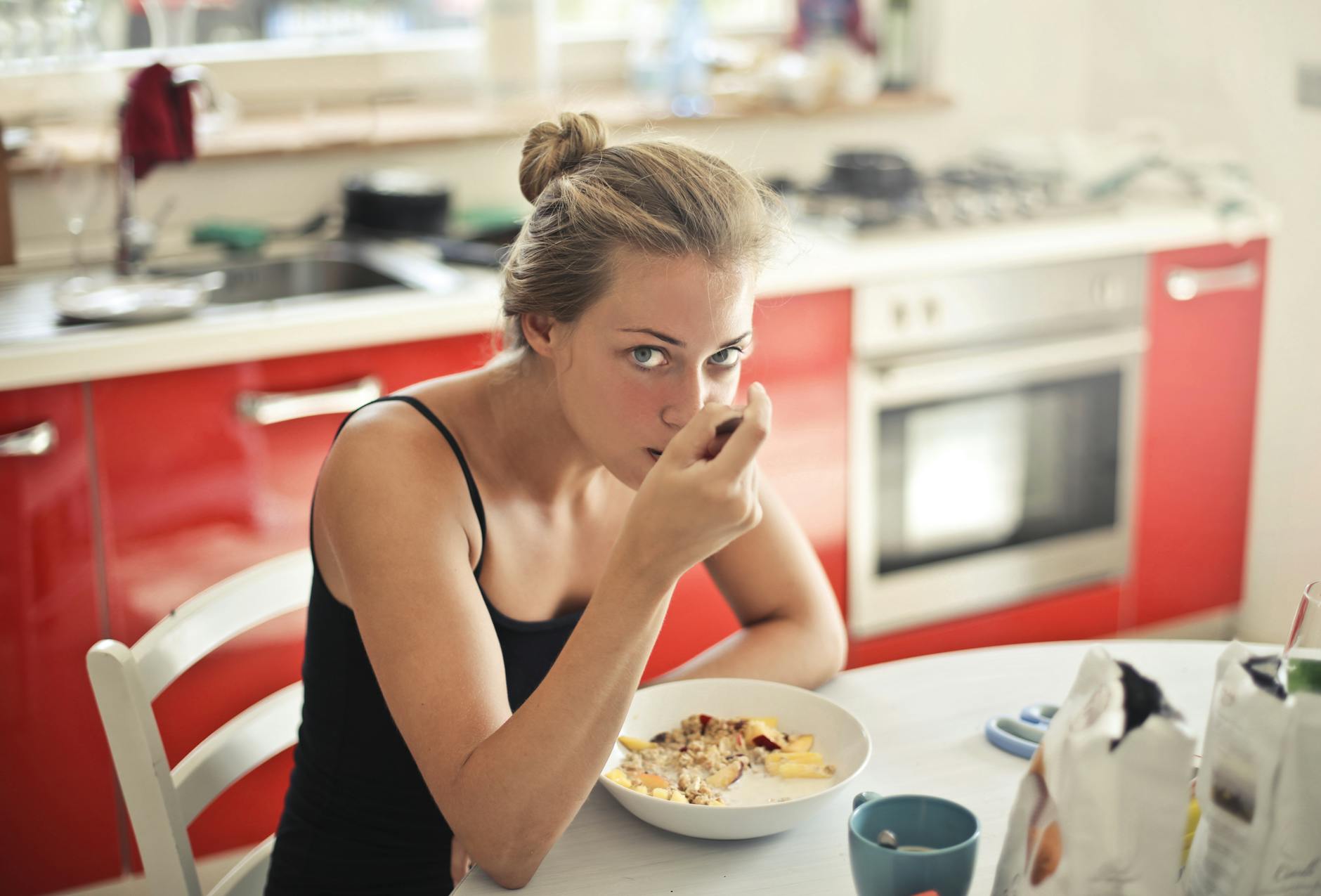 Femme mangeant un petit-déjeuner sain avec des céréales et du lait à une table de cuisine.